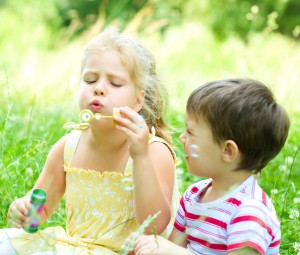 Cute girl and boy blowing soap bubbles, outdoors